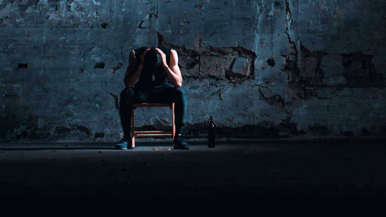 niedergeschlagener Mann auf einem Stuhl in einem dunklen Raum