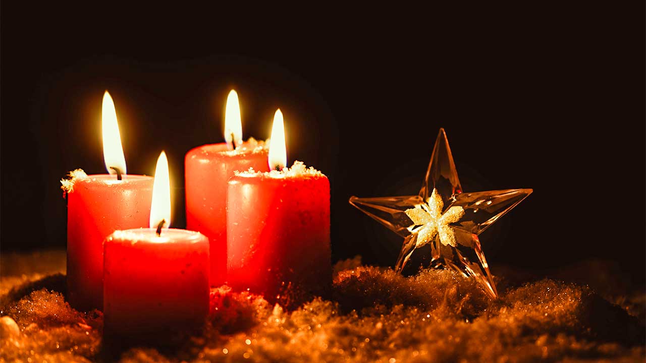 vier brennende Adventskerzen mit einem Weihnachtsstern nebendran