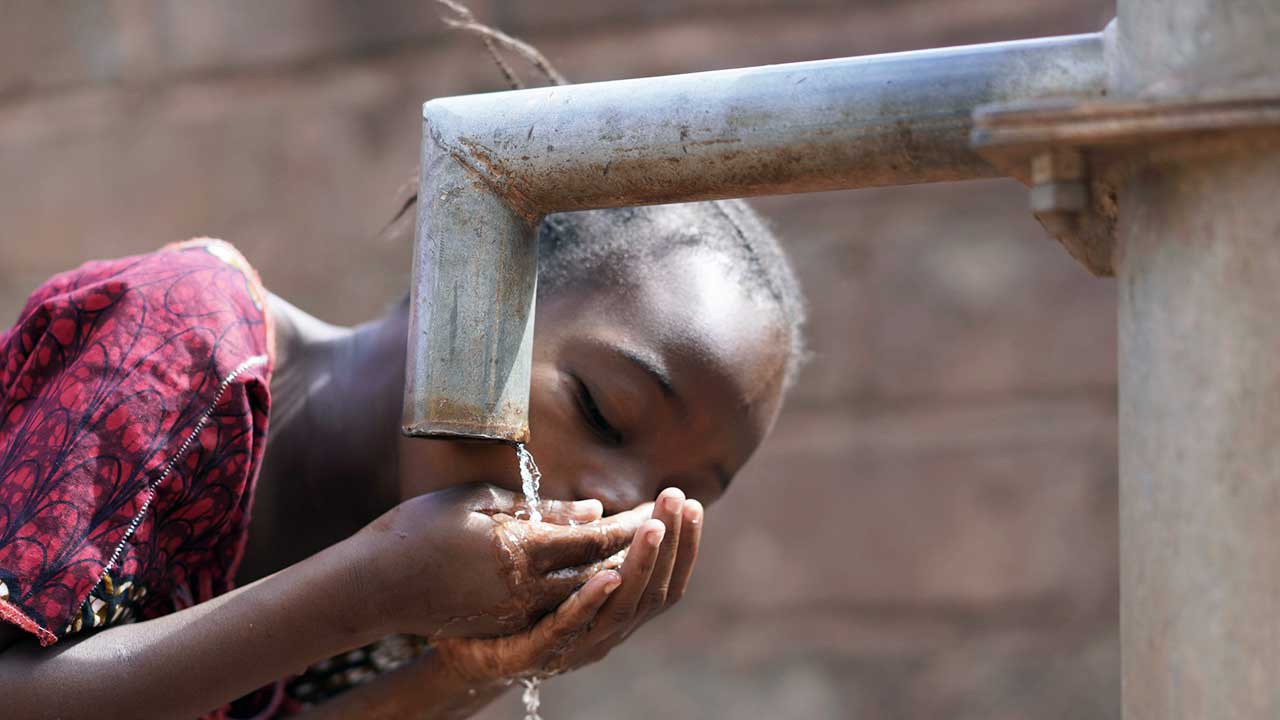 Afrikanisches Mädchen trinkt Wasser ab einer Röhre