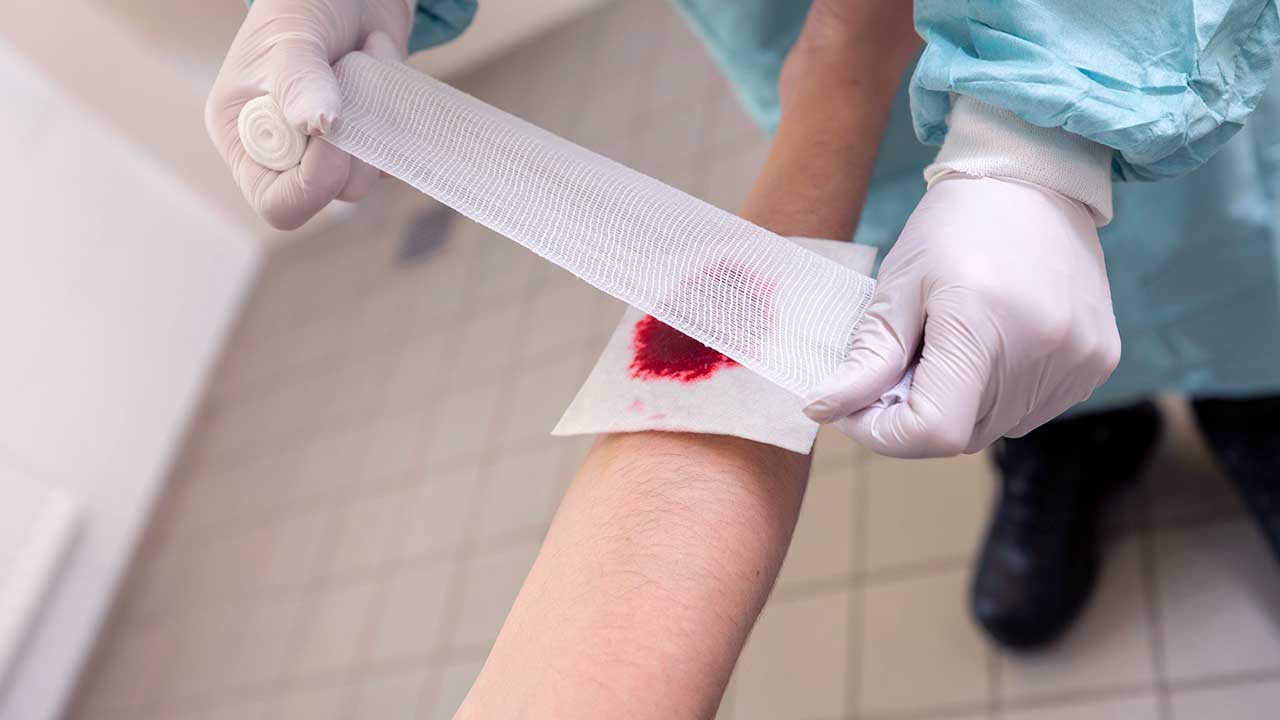 Arzt verbindet eine blutende Wunde auf einem Arm