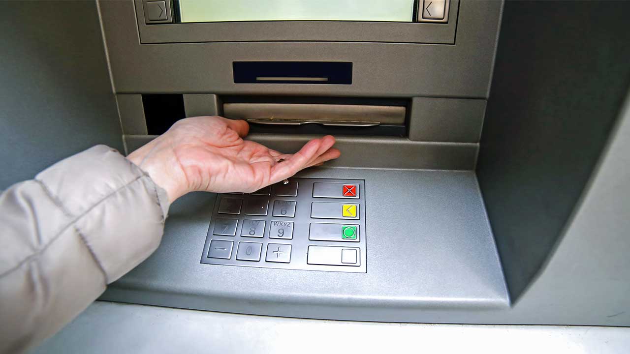 Hand wartet bei einem Bankomat auf die Ausgabe von Geldscheinen