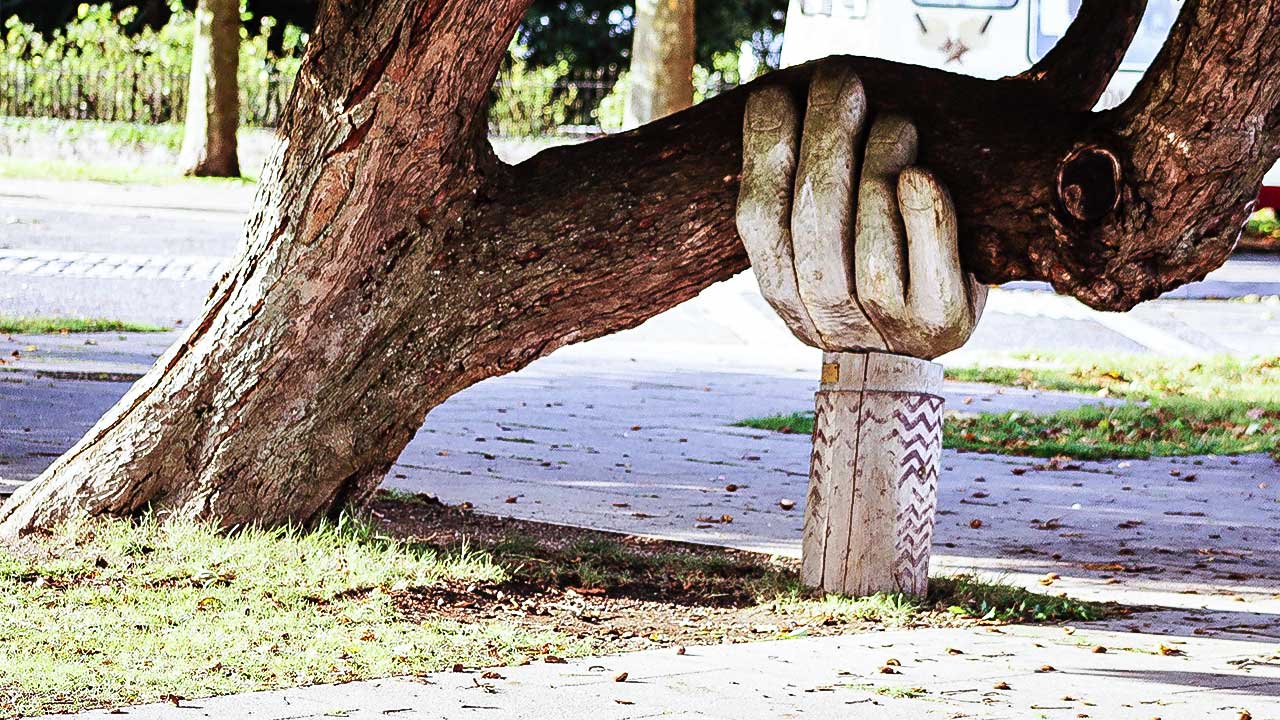 Eine Hand aus Holz stützt einen Baum, der waagrecht wächst