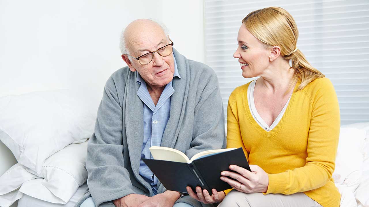Frau mittleren Alters liest einem Senior aus einem Buch vor