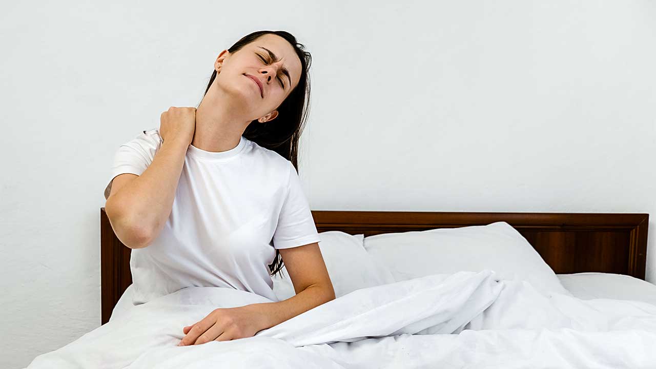junge Frau sitzt aufrecht im Bett und hat Gelenk- oder Muskelschmerzen