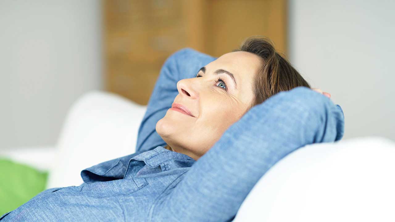 Frau liegt lächelnd auf einem Sofa und blickt nach Oben