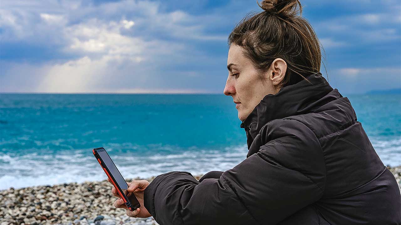 Frau sitzt am Strand und blickt auf ihr Smartphone