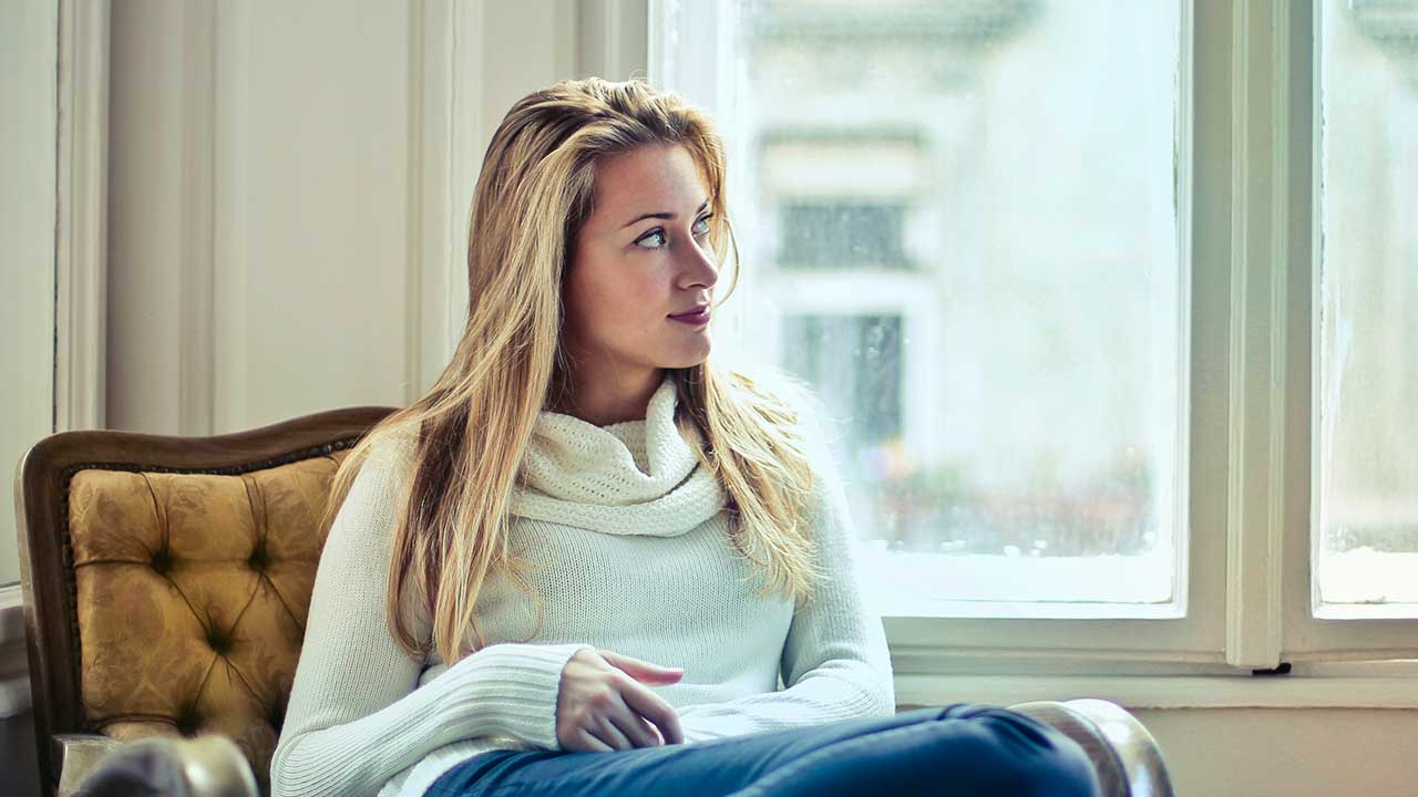 jüngere Frau sitzt entspannt vor einem Wohnzimmerfenster