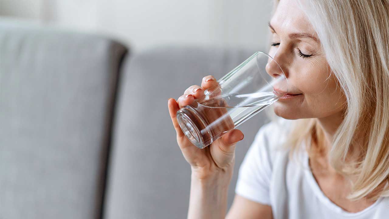 Frau sitzt auf einem Sofa und trinkt Wasser