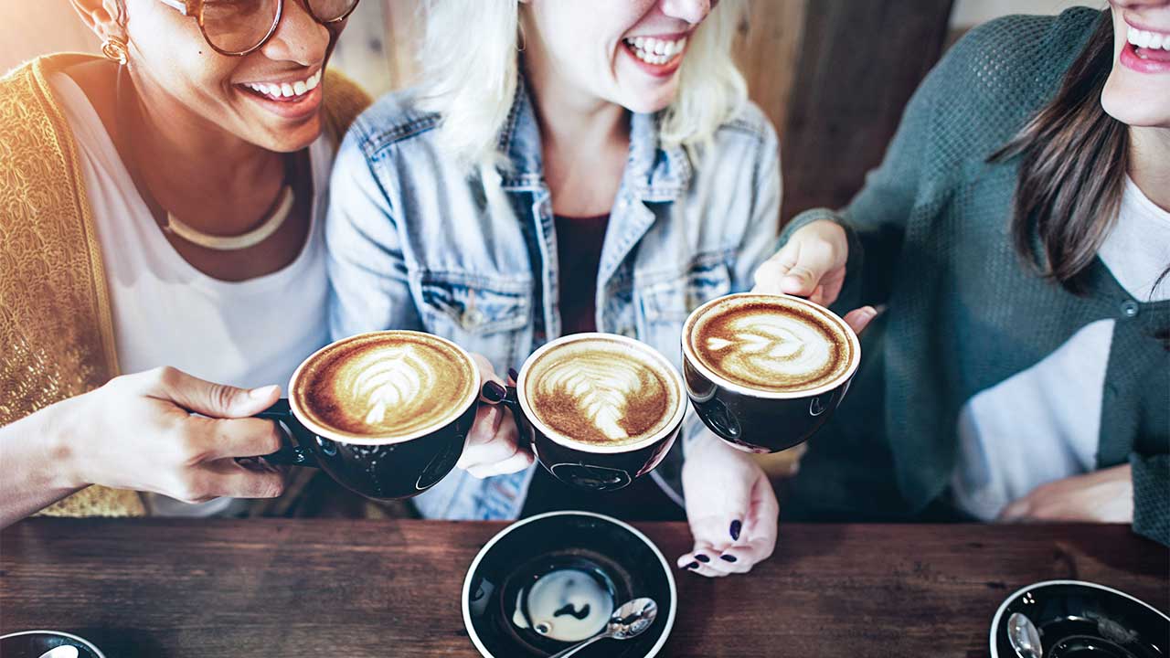 drei Frauen mit je einer Kaffeetasse stossen fröhlich an