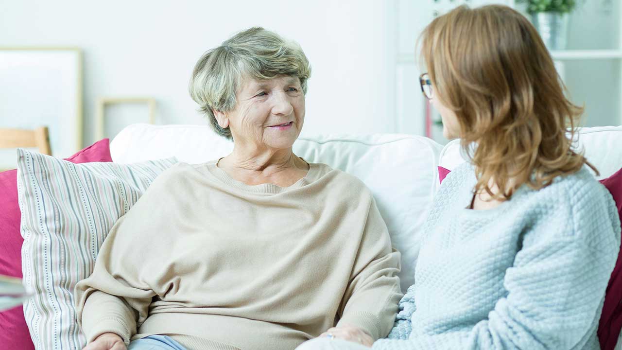 Gespräch zwischen Seniorin und jüngerer Frau auf einem Sofa