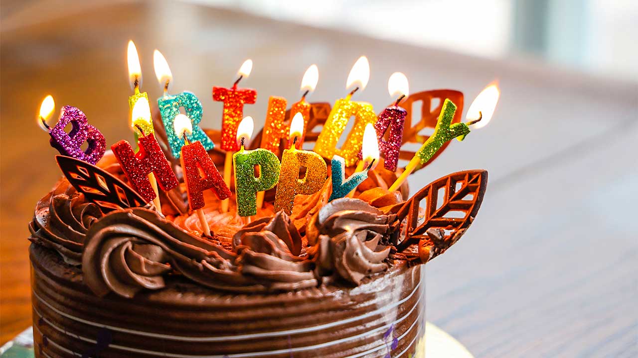 Geburtstagskuchen, auf dem mit Kerzen Happy Birthday geschrieben ist