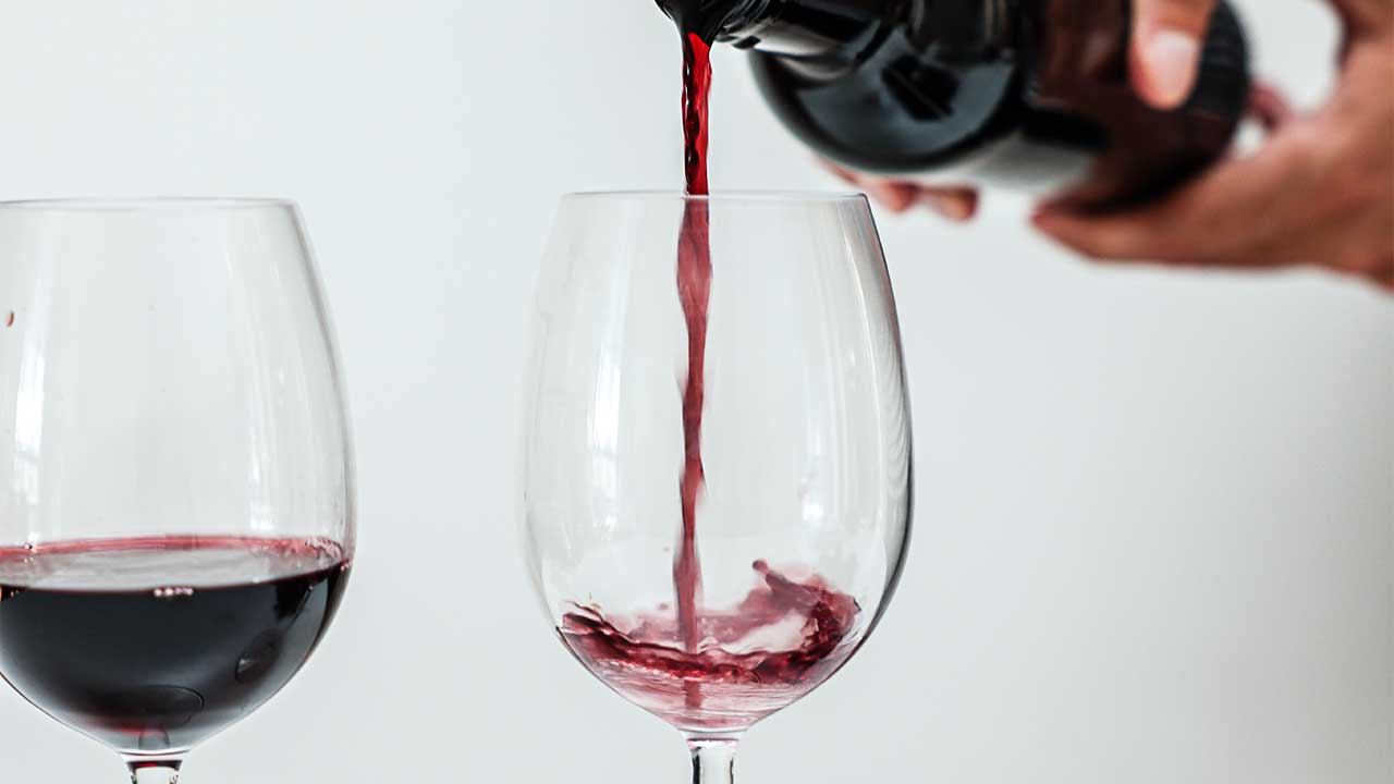 In einem Glas wird Rotwein eingeschenkt