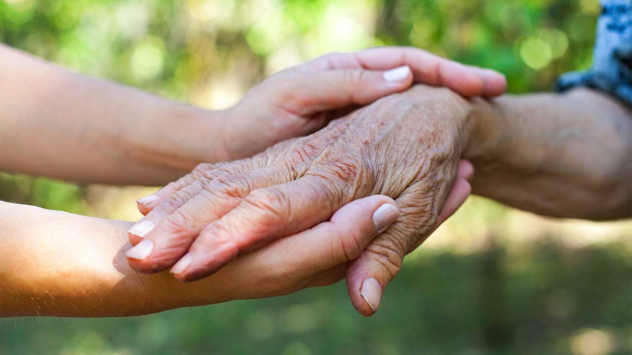 jüngere Frau hält mit ihren Händen die Hand einer Seniorin