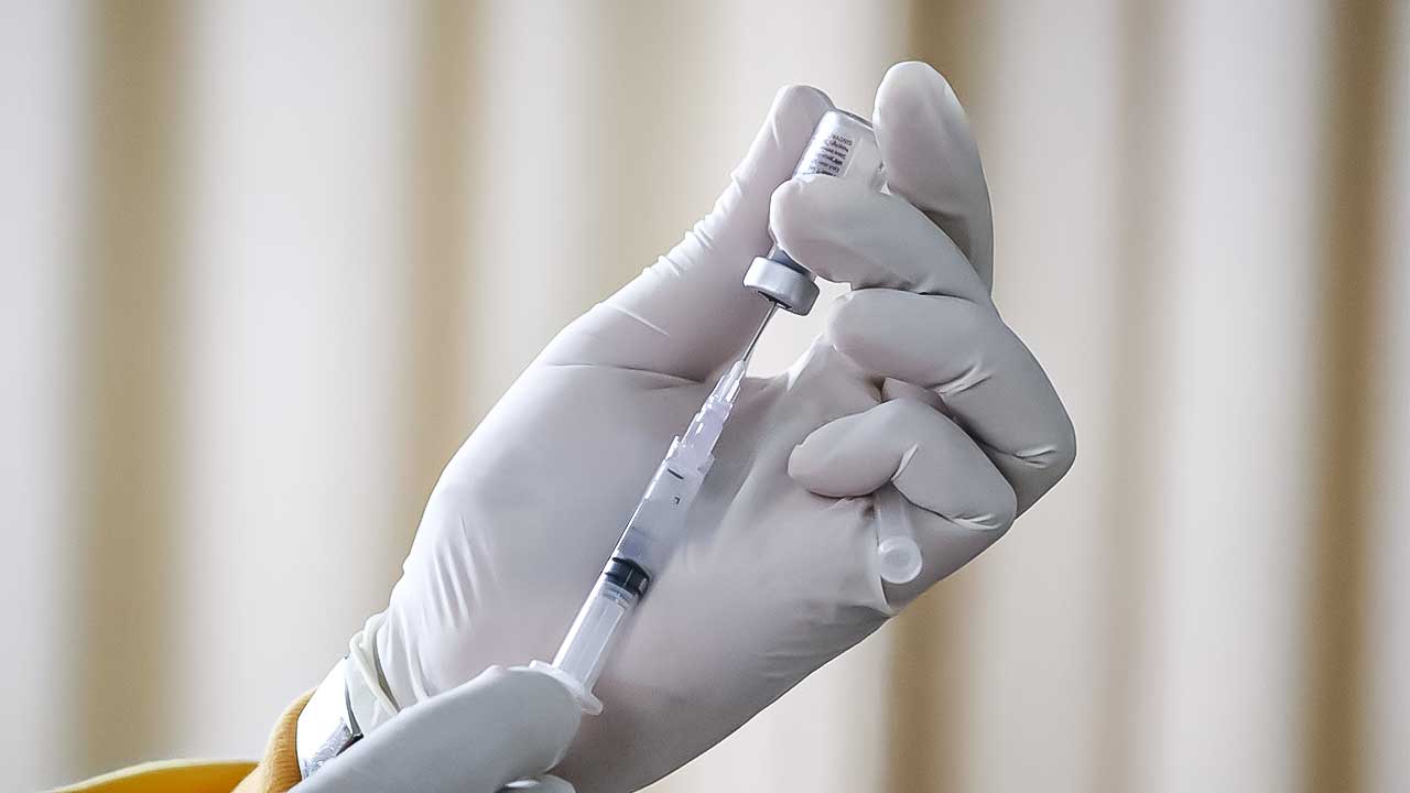 Hand in Gummihandschuh hält Spritze und Impffläschchen