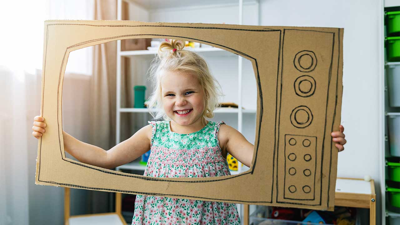 Mädchen blickt durch einen Fernseher aus Karton und hat Spass