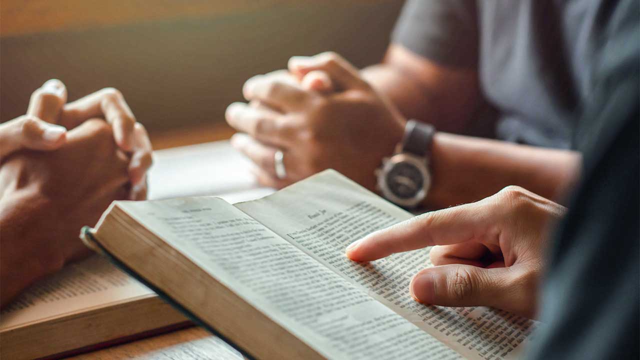 Blick auf Hände von Teilnehmern einer Kleingruppe, eine Bibel ist geöffnet