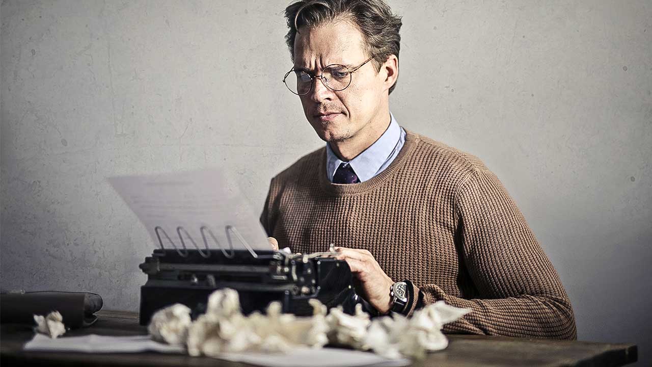 Mann an einer Schreibmaschine mit zerknüllten Blättern