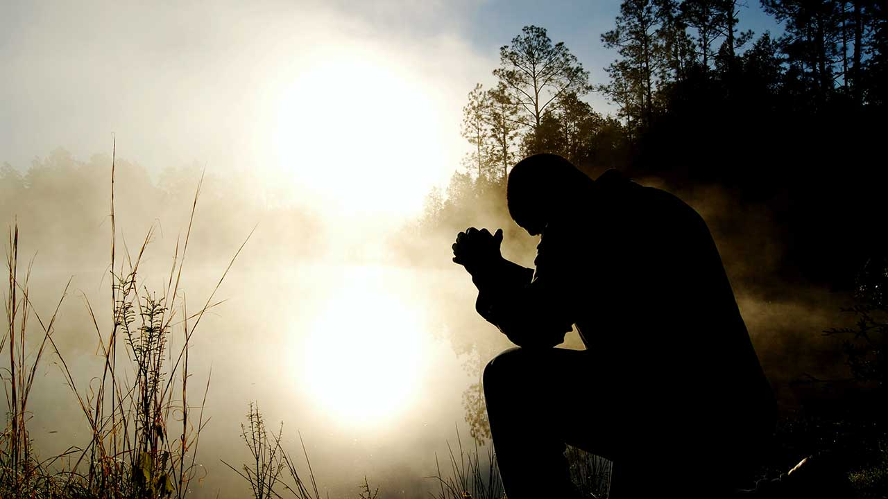 Mann als Silhouette an einem Weiher betet