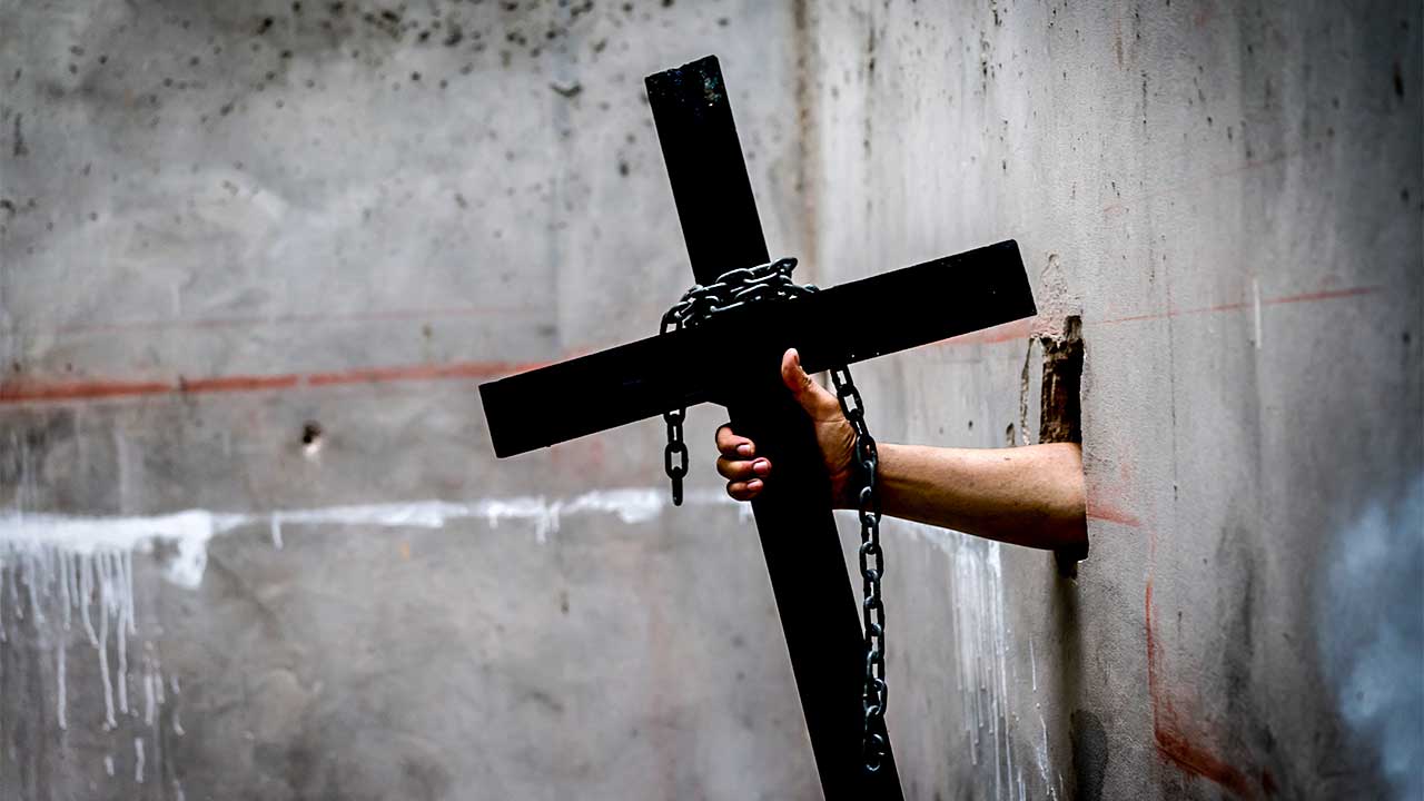 Hand aus einer Mauer hält ein Kreuz