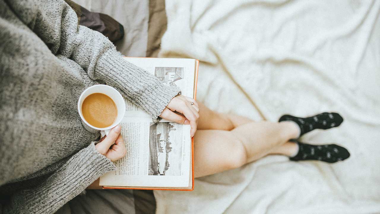 Eine Frau geniesst ihre Ruhe mit einem Kaffee und einem Buch in der Hand