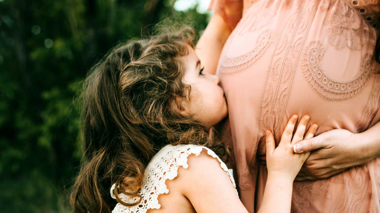 Mädchen küsst den Bauch ihrer schwangeren Mutter