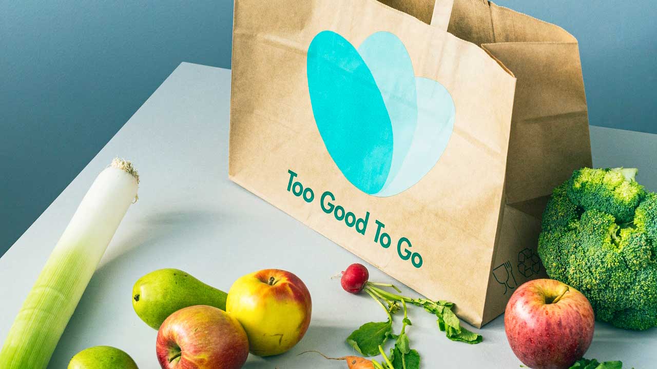 Papiertasche mit Logo von «Too Good To Go», umgeben von Früchten und Gemüse