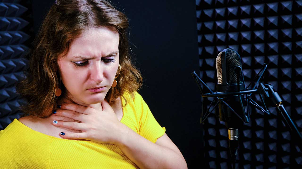 junge Frau in einem Aufnahmestudio hält sich einen Hand an den Hals, weil die Stimme noch nicht richtig tönt