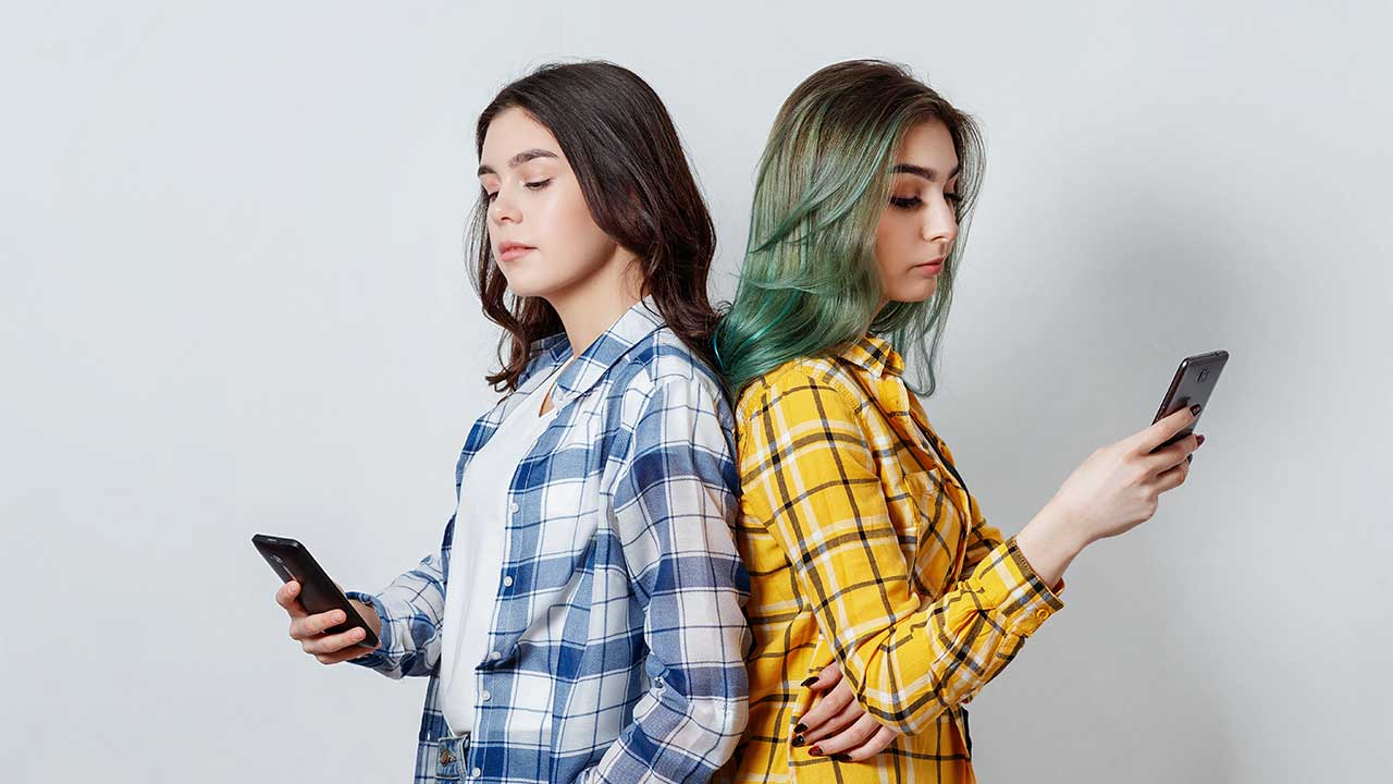 Zwei junge Frauen mit Smartphones stehen Rücken an Rücken